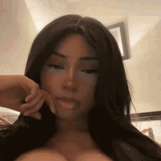 a woman with long dark hair is making a funny face with her hand on her chin .