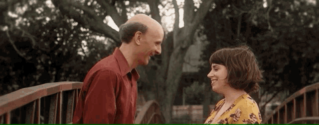 a man in a red shirt and a woman in a yellow shirt are looking at each other on a bridge