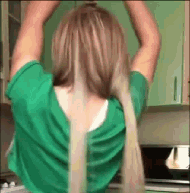 a woman in a green shirt is holding her hair up