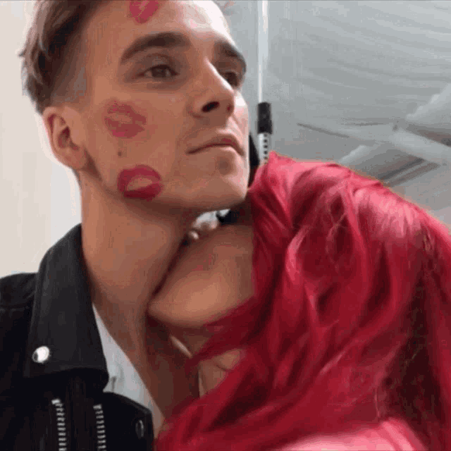 a woman with red hair is kissing a man with lipstick on his face