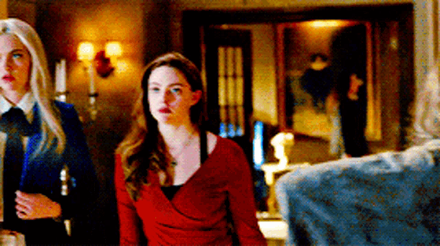 two women are standing next to each other in a room and one is wearing a red dress .