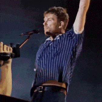 a man in a blue and white striped shirt is singing into a microphone on stage .