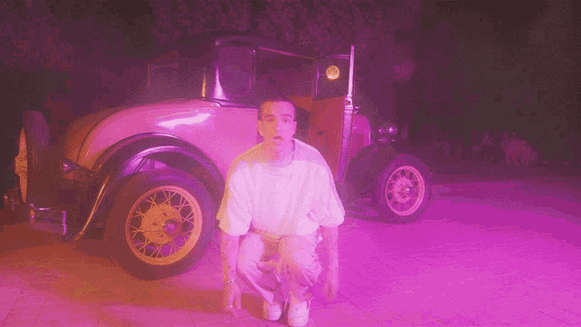 a man kneeling in front of a car with a purple light behind him
