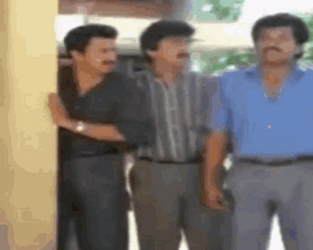 three men are standing next to each other and one of them has a mustache .
