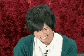 a man with black hair is smiling and wearing a green sweater and a white shirt .