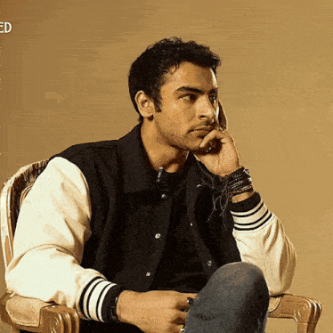 a man in a varsity jacket sits in a chair