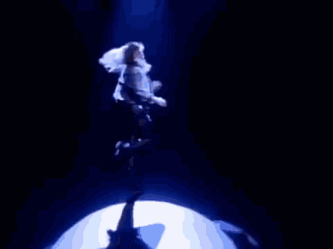 a woman is dancing on a stage in a dark room with a blue light behind her .