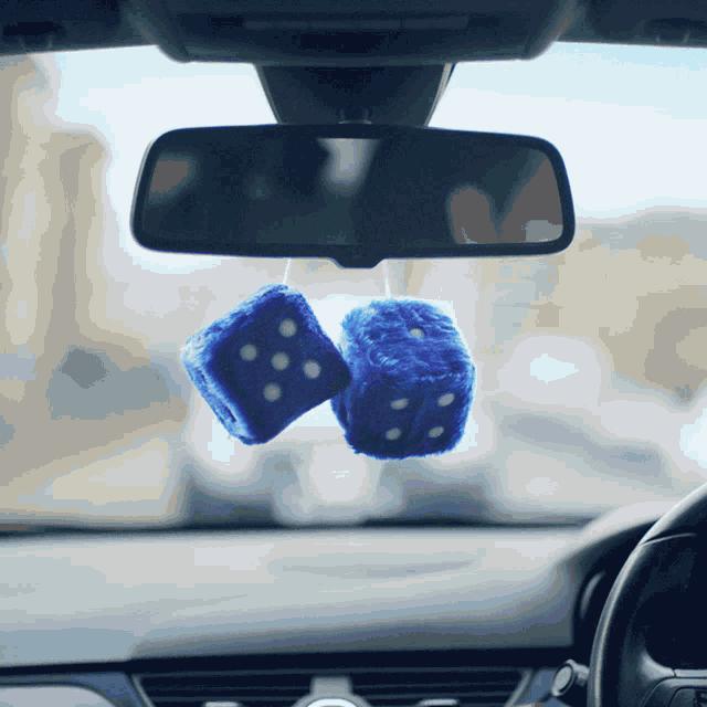 a pair of blue fuzzy dice hanging from a car rear view mirror
