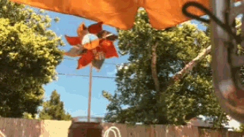 a windmill is hanging from an orange umbrella in the backyard
