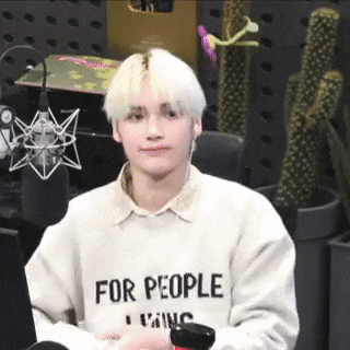 a young man with blonde hair is wearing a sweater that says `` for people '' while sitting in front of a microphone .