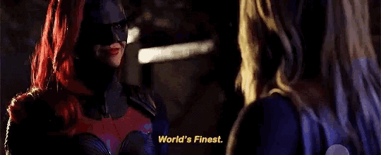 two women in superhero costumes are standing next to each other in a dark room .