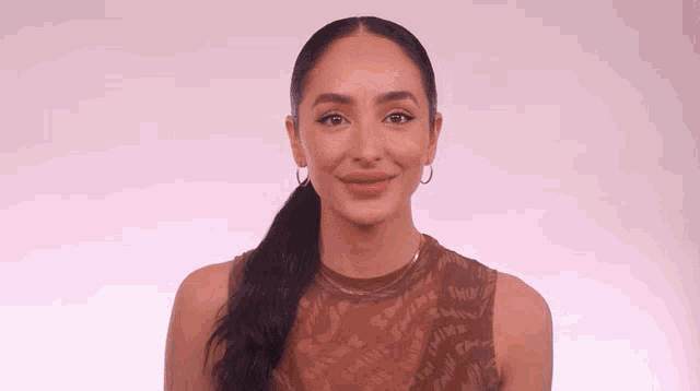 a woman with a ponytail and hoop earrings looks at the camera with a smile on her face