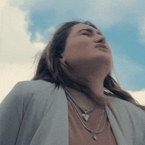 a woman wearing a necklace with a heart shaped pendant looks up at the sky