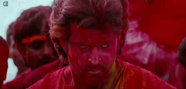 a man with red powder on his face is standing in front of a crowd of people .