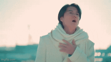 a man in a white coat and scarf is standing with his hands on his chest and looking up .