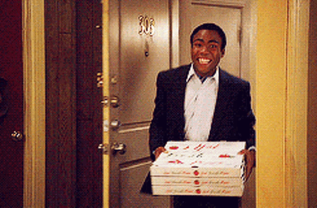 a man in a suit is carrying a stack of pizza boxes and smiling