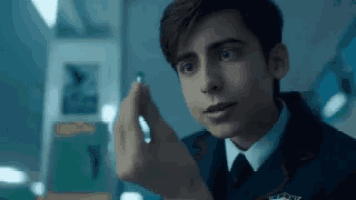 a young man in a suit and tie is holding a small green object in his hand