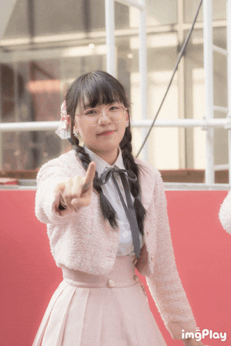 a girl wearing glasses and a pink dress is pointing at the camera with imgplay written on the bottom right