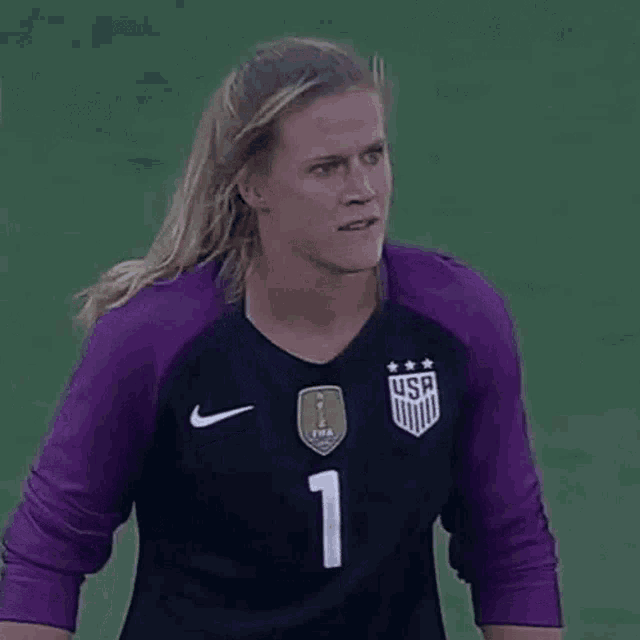 a female soccer goalie wearing a purple jersey is standing on the field .