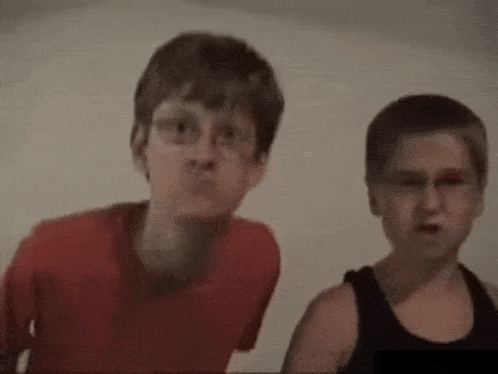 two young boys are standing next to each other looking at the camera .