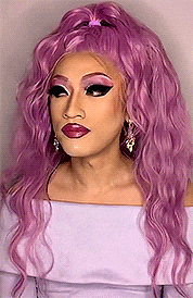 a woman with purple hair and purple makeup is wearing a purple top and earrings .