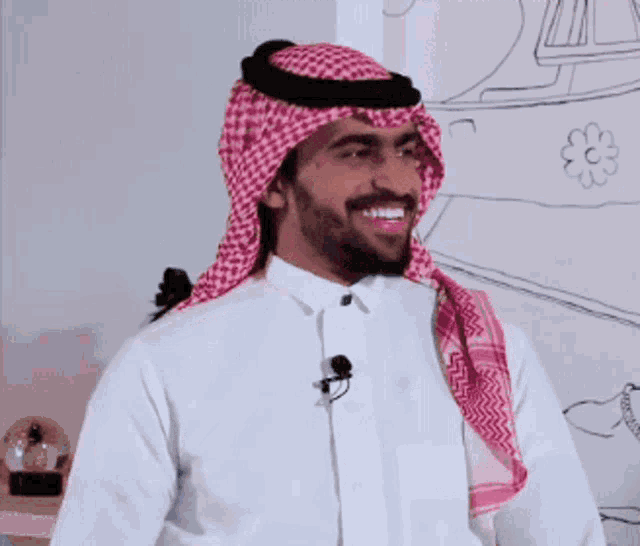 a man wearing a white shirt and a red and white head scarf is smiling