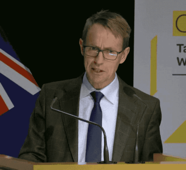 a man in a suit and tie stands at a podium with two microphones