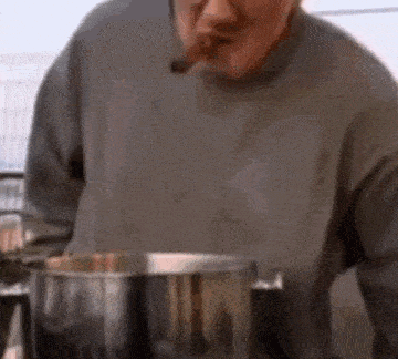 a man is smoking a cigar in front of a pot of food .