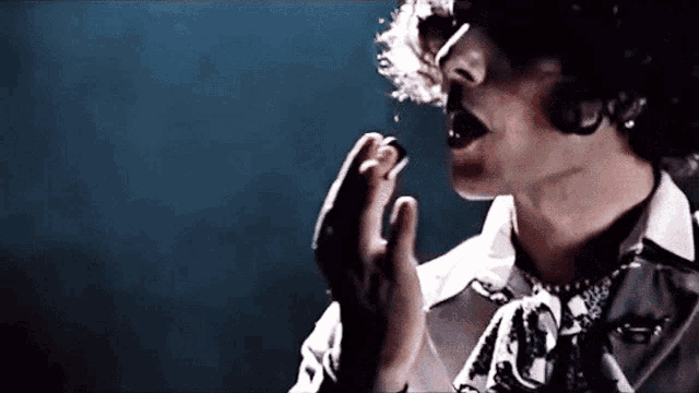 a man with curly hair is singing into a microphone while wearing sunglasses .