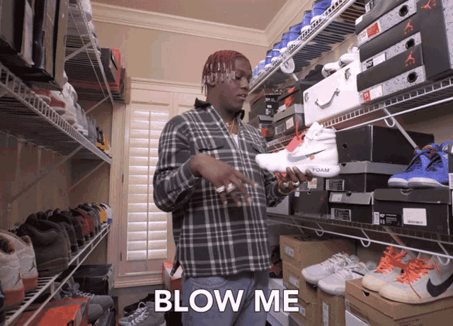 a man in a plaid shirt is holding a pair of nike shoes and the word blow me is above him