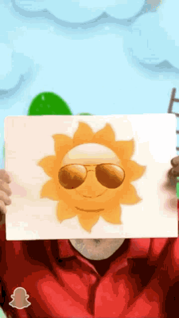 a man in a red shirt holds up a picture of a smiling sun with sunglasses