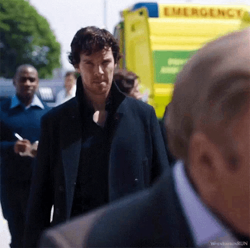 a man in a suit stands in front of an ambulance that says emergency