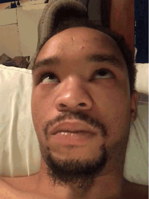 a man with a beard is laying on a bed and making a funny face