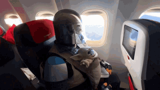 a person sitting on an airplane with a baby in a carrier that says norwegian on it