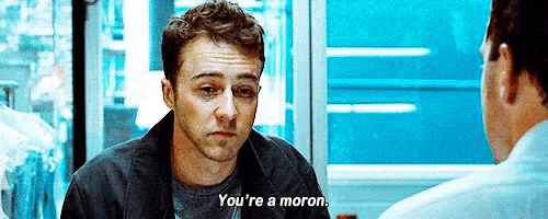 a man in a black jacket is talking to another man and says " you 're a moron "