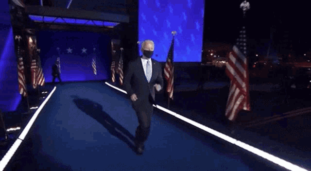 a man in a suit and tie is dancing on a stage with american flags behind him