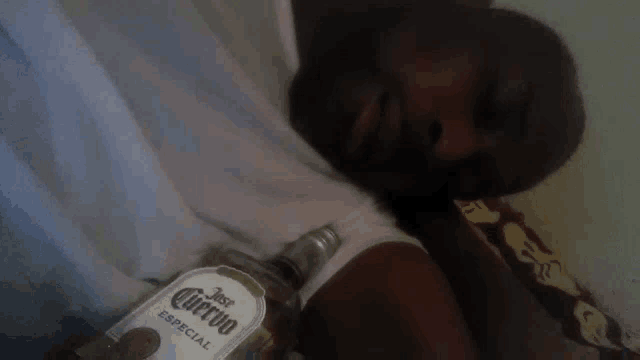 a man laying on a bed holding a bottle of jose cuervo