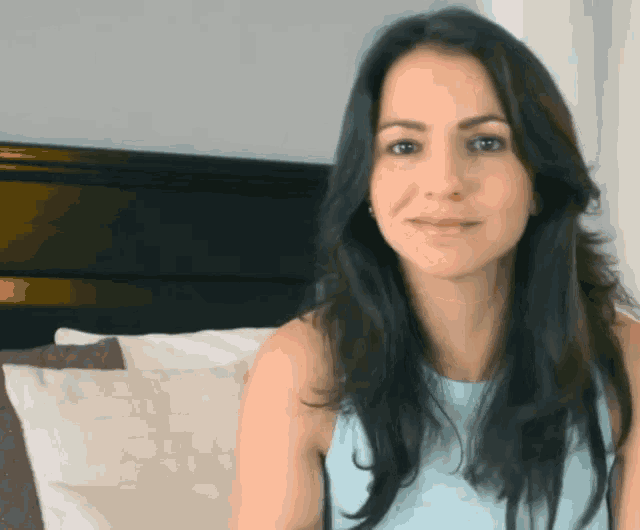 a woman with long dark hair is sitting on a bed