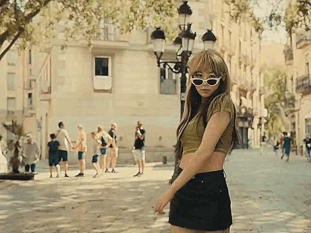 a woman wearing sunglasses and a crop top stands on a sidewalk