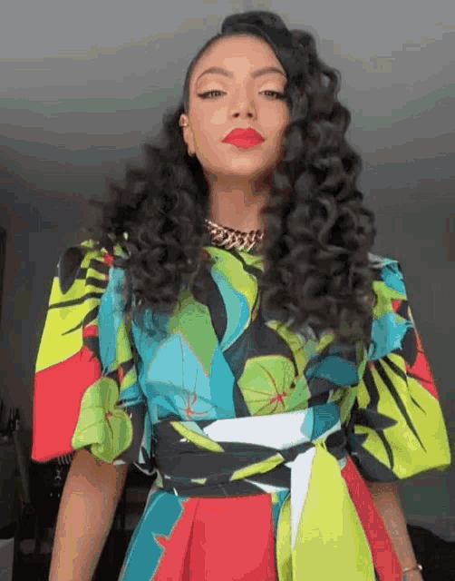 a woman with curly hair is wearing a colorful top