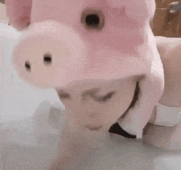 a woman is wearing a pink pig hat and a bow tie while laying in a bathtub .