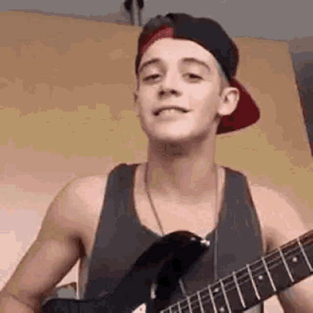 a young man is playing a guitar while wearing a hat .