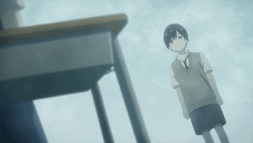 a boy in a vest and tie stands in front of a classroom desk