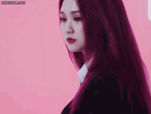 a woman with long purple hair is wearing a black suit and tie .