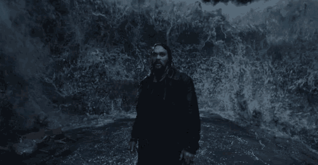 a man is standing in front of a large wave in the ocean .