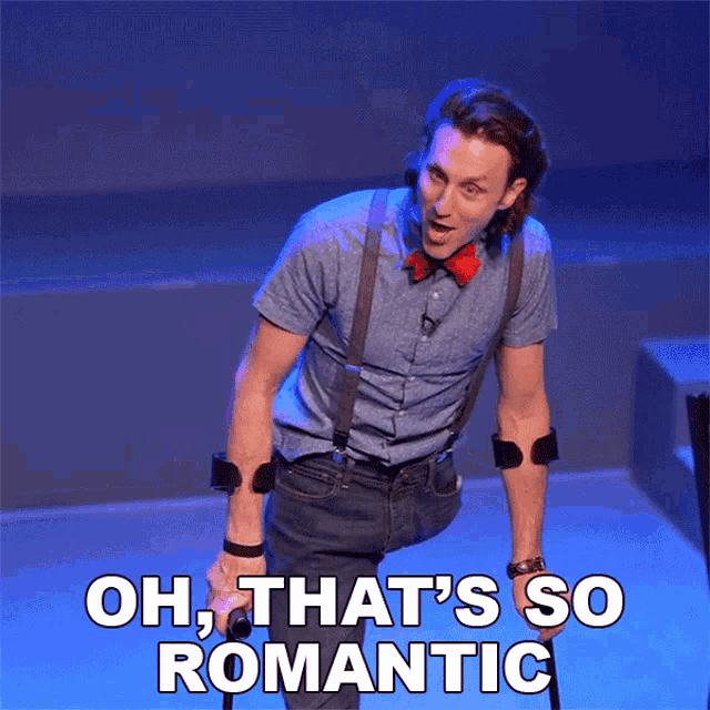 a man with a bow tie and suspenders stands on a stage with the words oh that 's so romantic above him