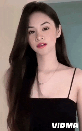 a woman with long dark hair is wearing a black tank top and a necklace .
