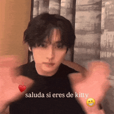 a young man is making a heart shape with his hands and says " saluda si eres de kitty " in the corner
