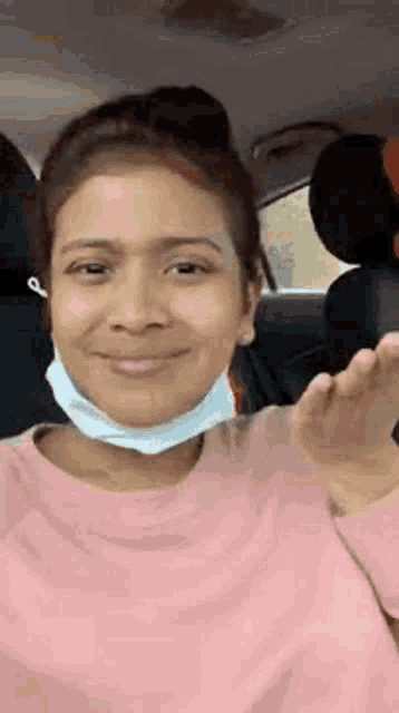 a woman wearing a face mask is sitting in the back seat of a car and waving .