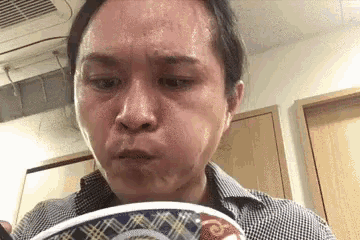 a man is eating a bowl of food with his mouth open and sweating .